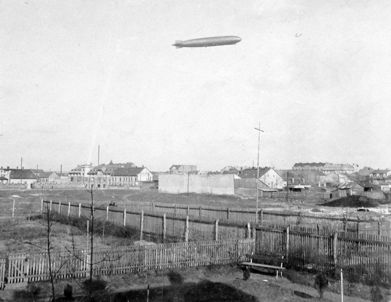 szemben a Telepes utca épületei a Limanova tér irányából nézve, a magasban a D-LZ127 Graf Zeppelin léghajó.