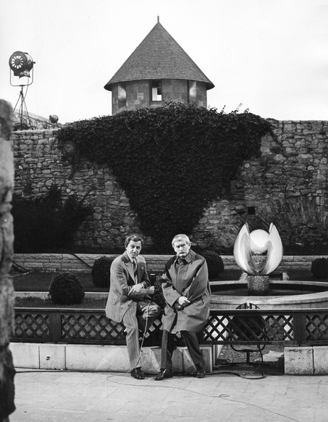 MTV Művészeti Magazin felvétele a Királyi Palota déli zárt udvarában. Kovalik Károly riporter és Borsos Miklós szobrászművész. Háttérben a szobrász 1968-ban alkotott műve a Virágidomú vízköpő.